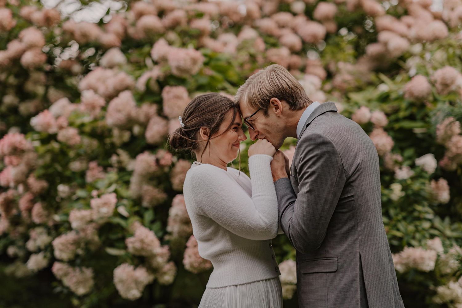 An intimate wedding moment captured near blooming pink rose bushes in a garden setting.
