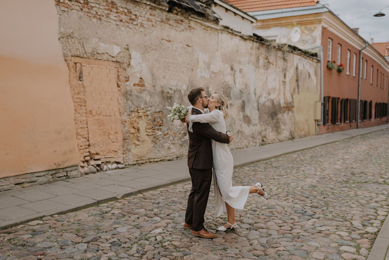 Newlyweds walking and embracing on a cobblestone street with historic walls.