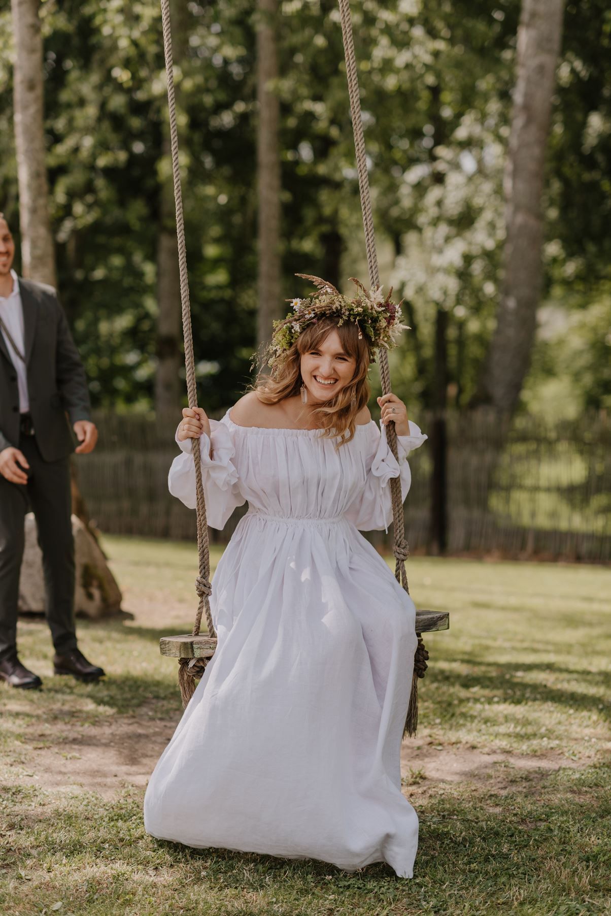 A quaint outdoor scene featuring a wooden rope swing adorned with white fabric in a garden setting.