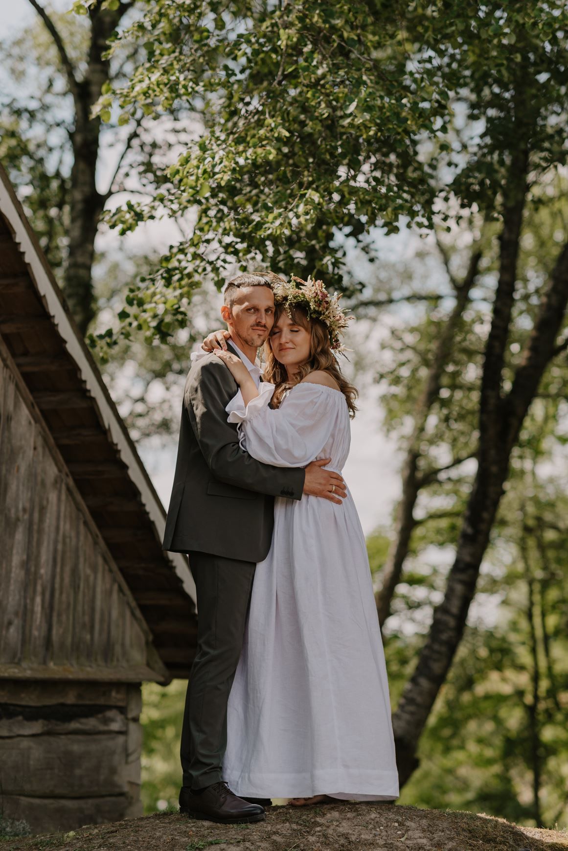A tender moment captured near a rustic wooden barn structure surrounded by lush greenery.
