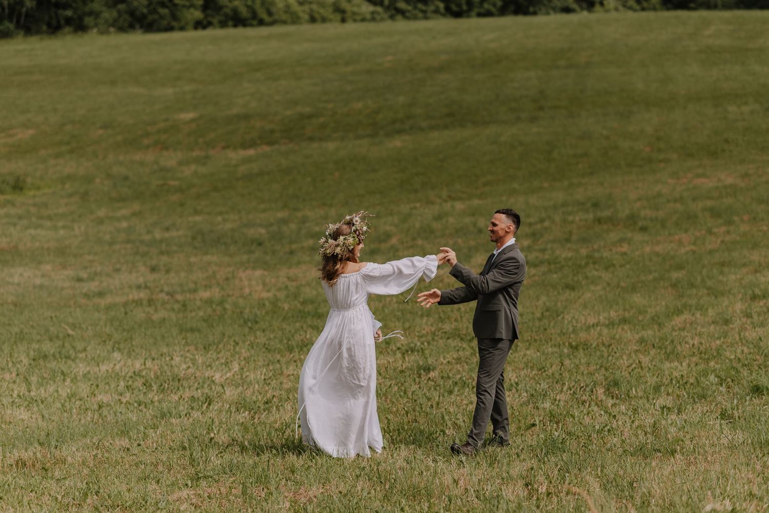 Wedding couple twirling and dancing together on a grassy lawn.