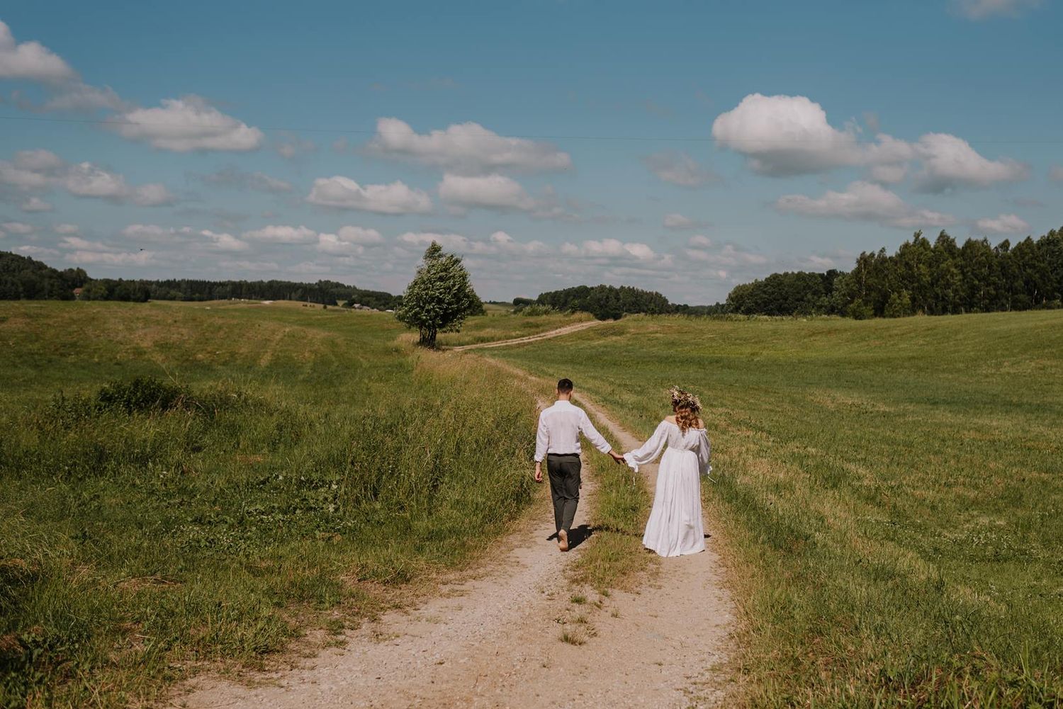 Panoramic view of a couple walking through rolling countryside under blue summer skies.