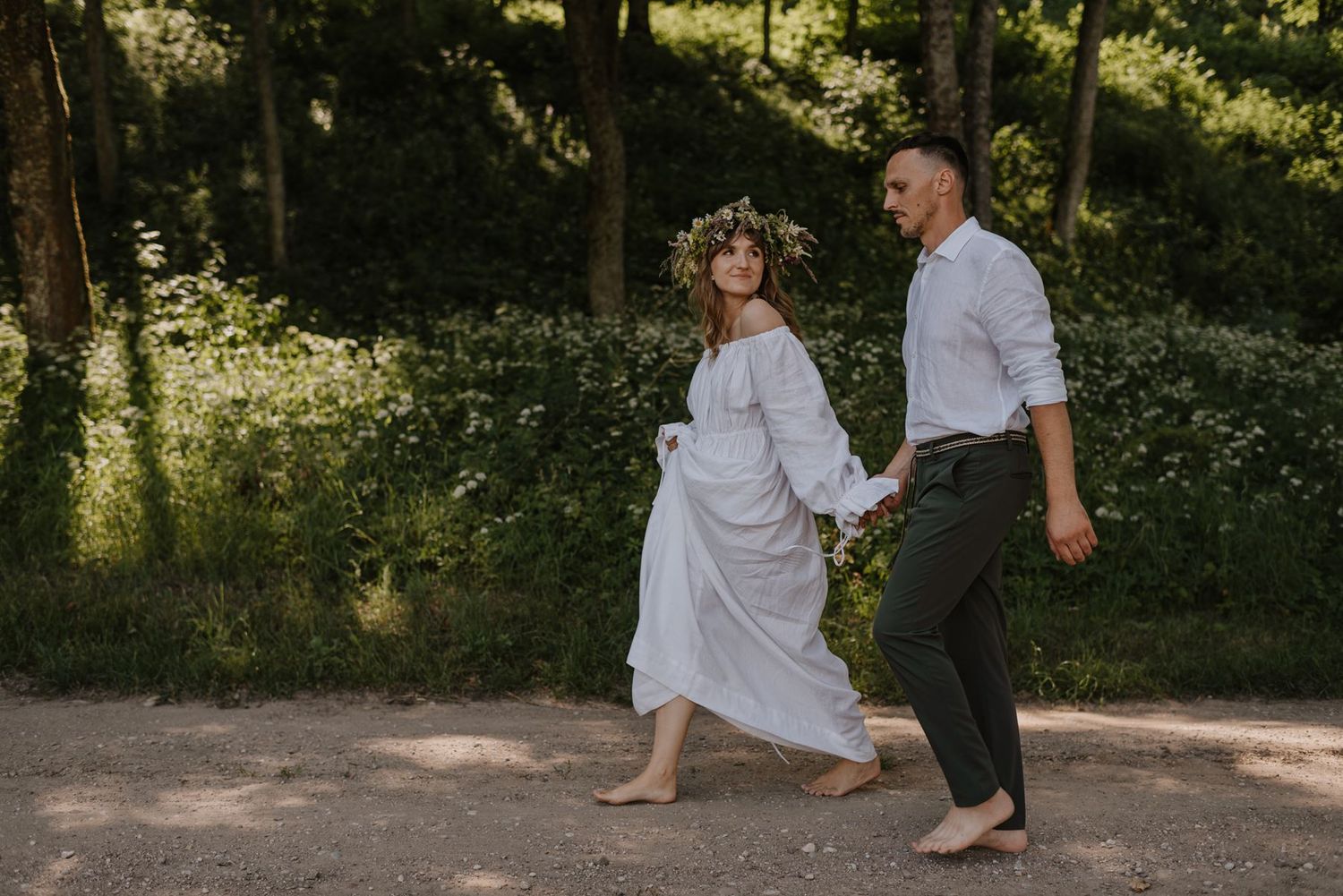 Wedding couple walking barefoot along a wooded path in golden sunlight.