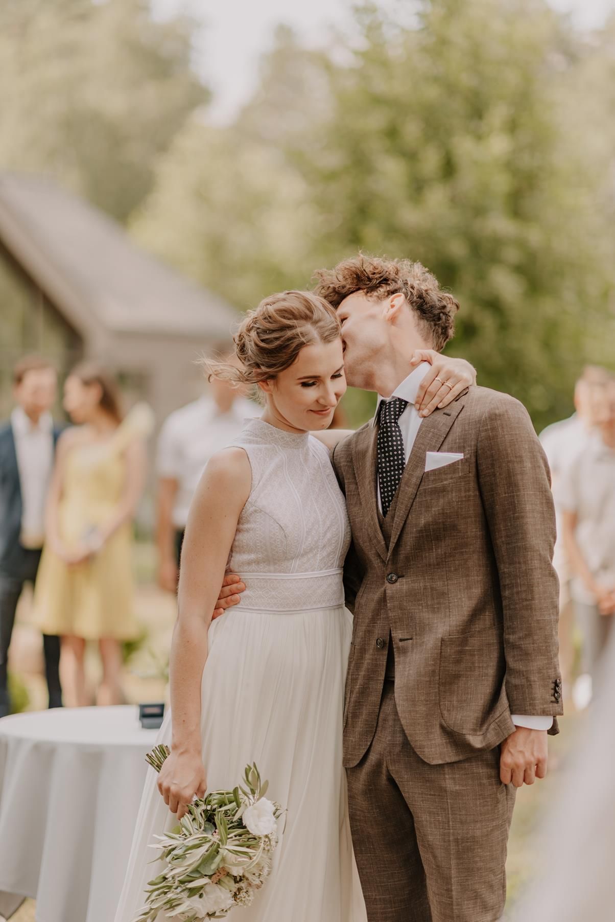 A tender moment between newlyweds in a garden setting with guests in the background.