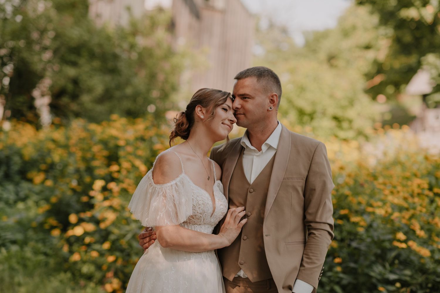 Bride and groom share intimate moments in a sunlit garden with yellow wildflowers.