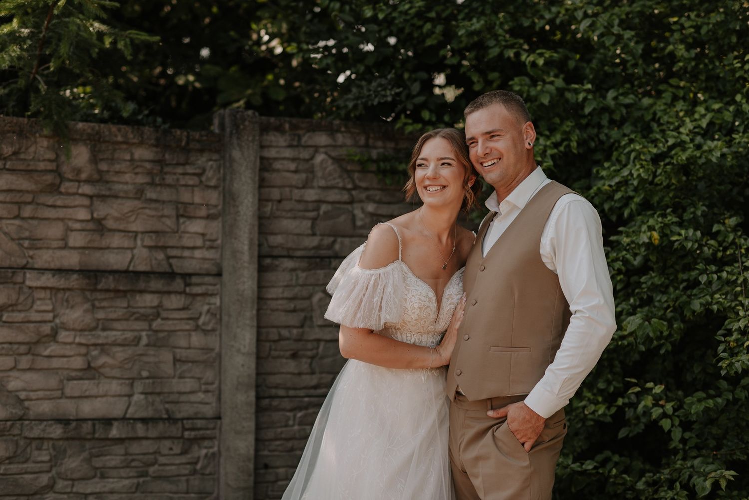 Wedding couple poses for romantic photos against a rustic stone wall backdrop.