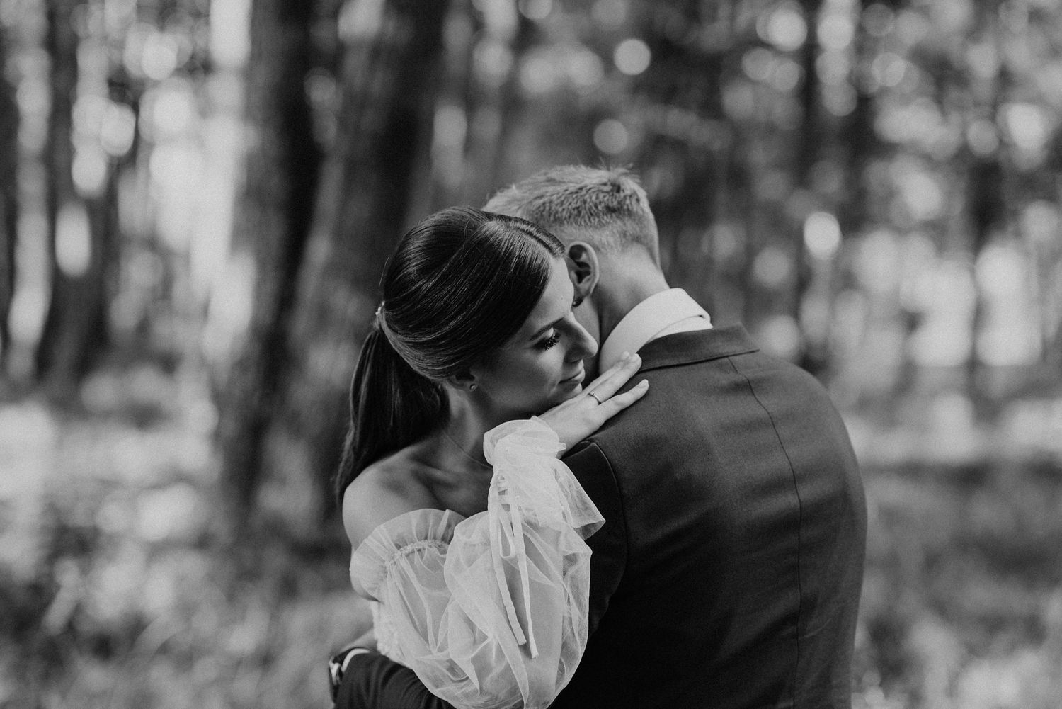 Intimate black and white wedding portrait captured in a forest setting.