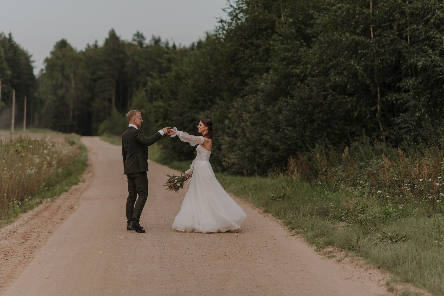 Couple walking down a scenic country dirt road surrounded by trees on their wedding day.