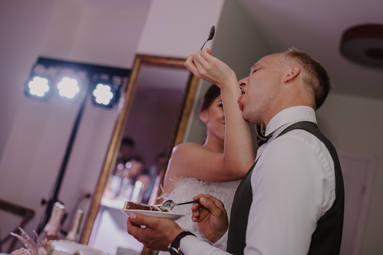 Newlyweds feeding each other wedding cake at their reception while dressed in formal attire.