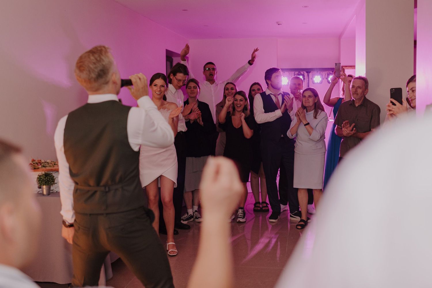 Wedding guests dancing and celebrating at a reception with pink lighting.