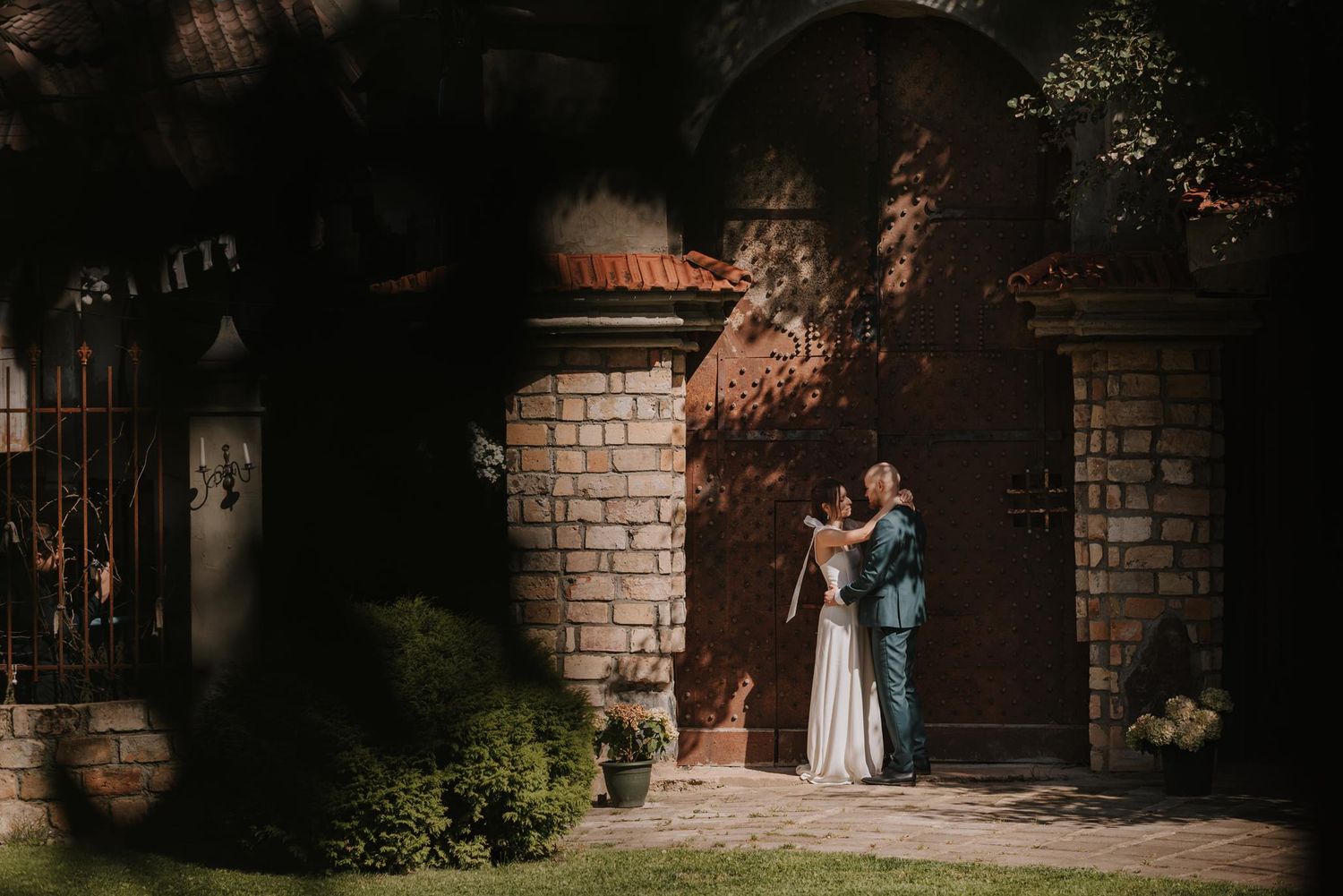 Wedding couple poses against rustic brick wall in dramatic lighting.