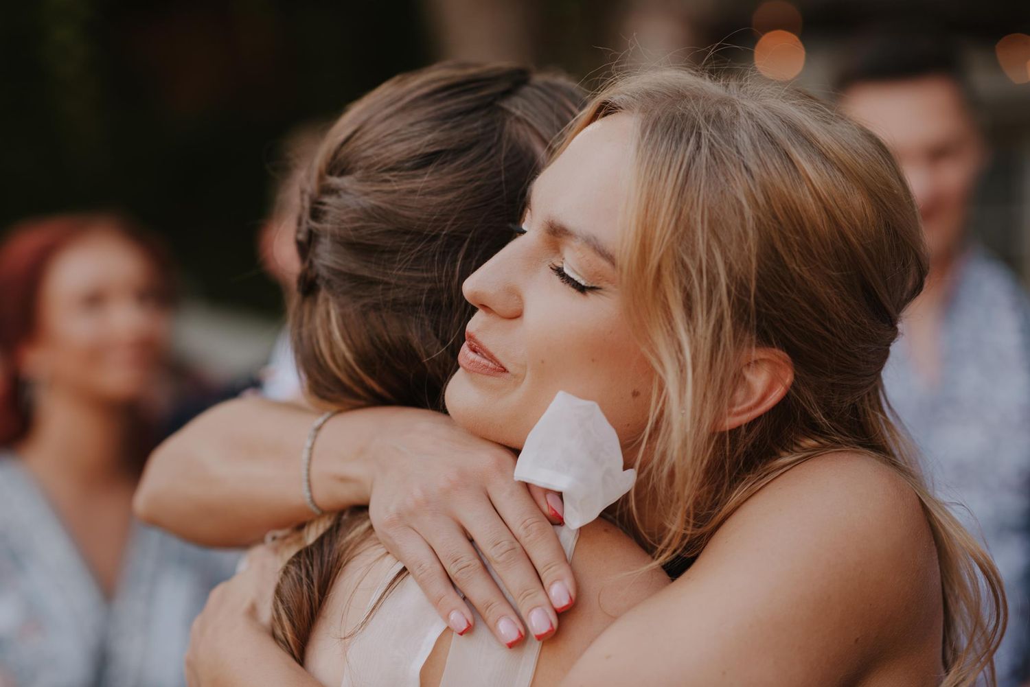 Wedding guests embrace emotionally during sunset reception outdoors.