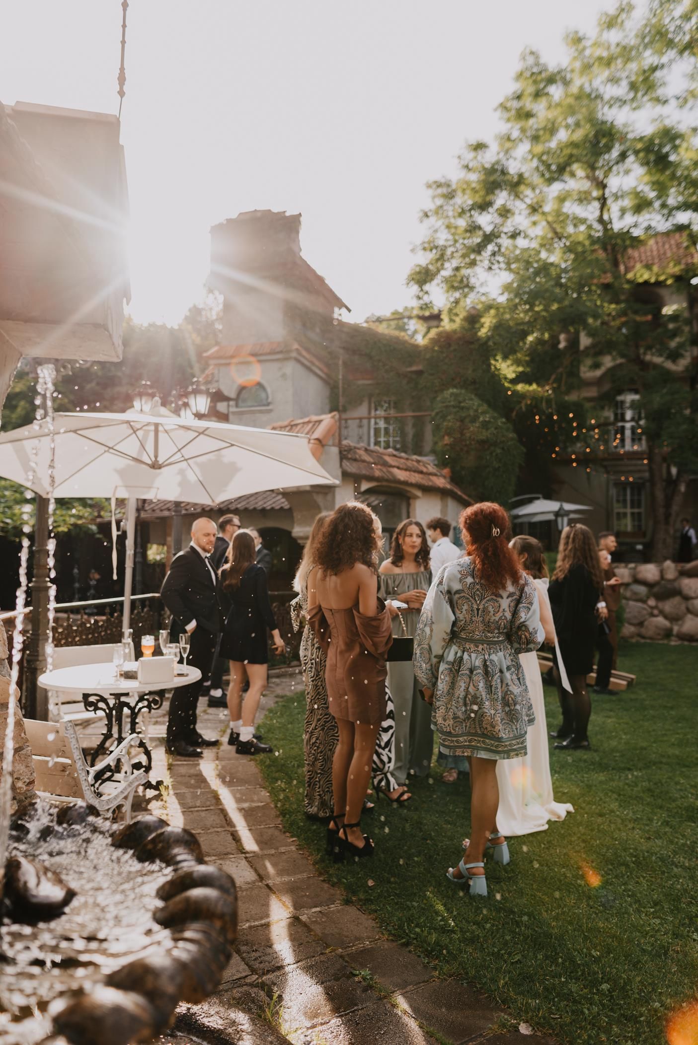 Outdoor wedding reception at sunset with guests mingling under white tents on a lawn.