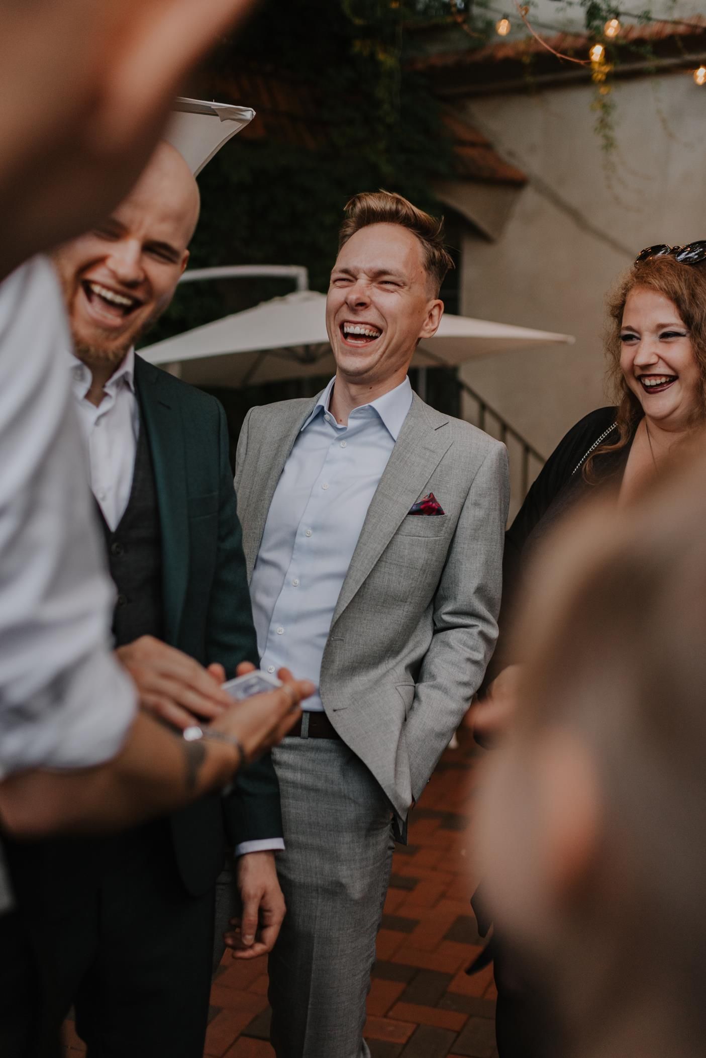 Wedding guests share laughter during reception in moody indoor lighting.