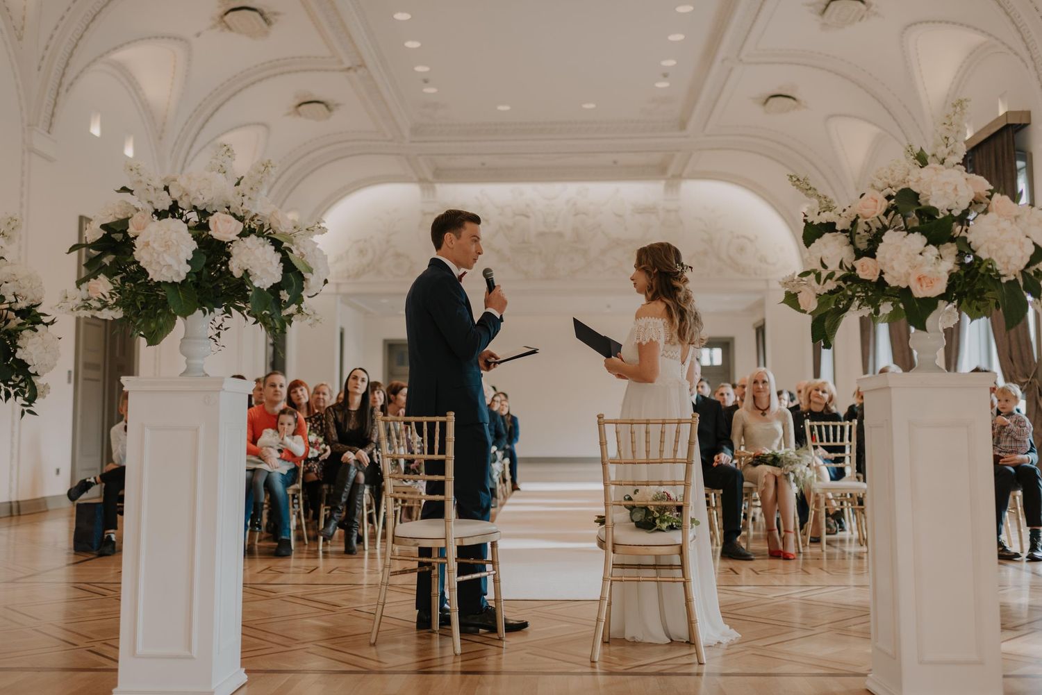 Elegant white wedding venue interior with ornate columns and floral decorations.