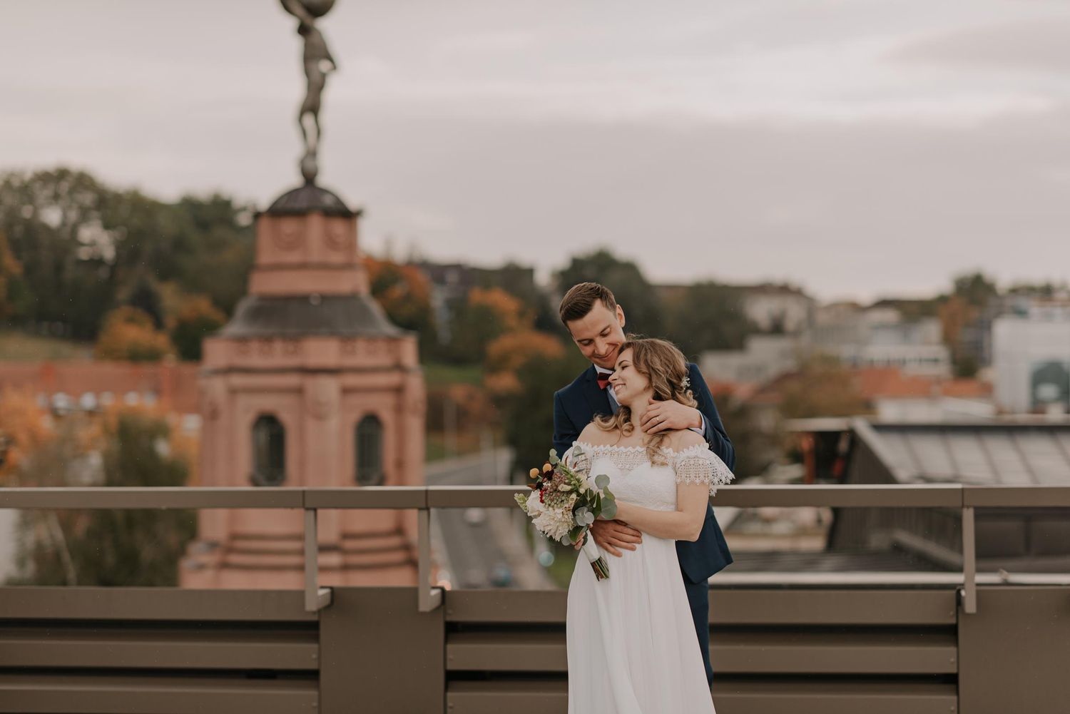 Wedding couple poses on rooftop terrace with city architecture in background.