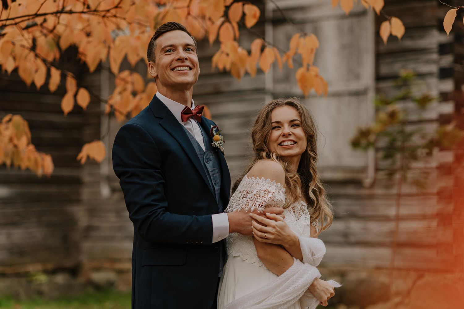Wedding couple laughs together against backdrop of autumn foliage.