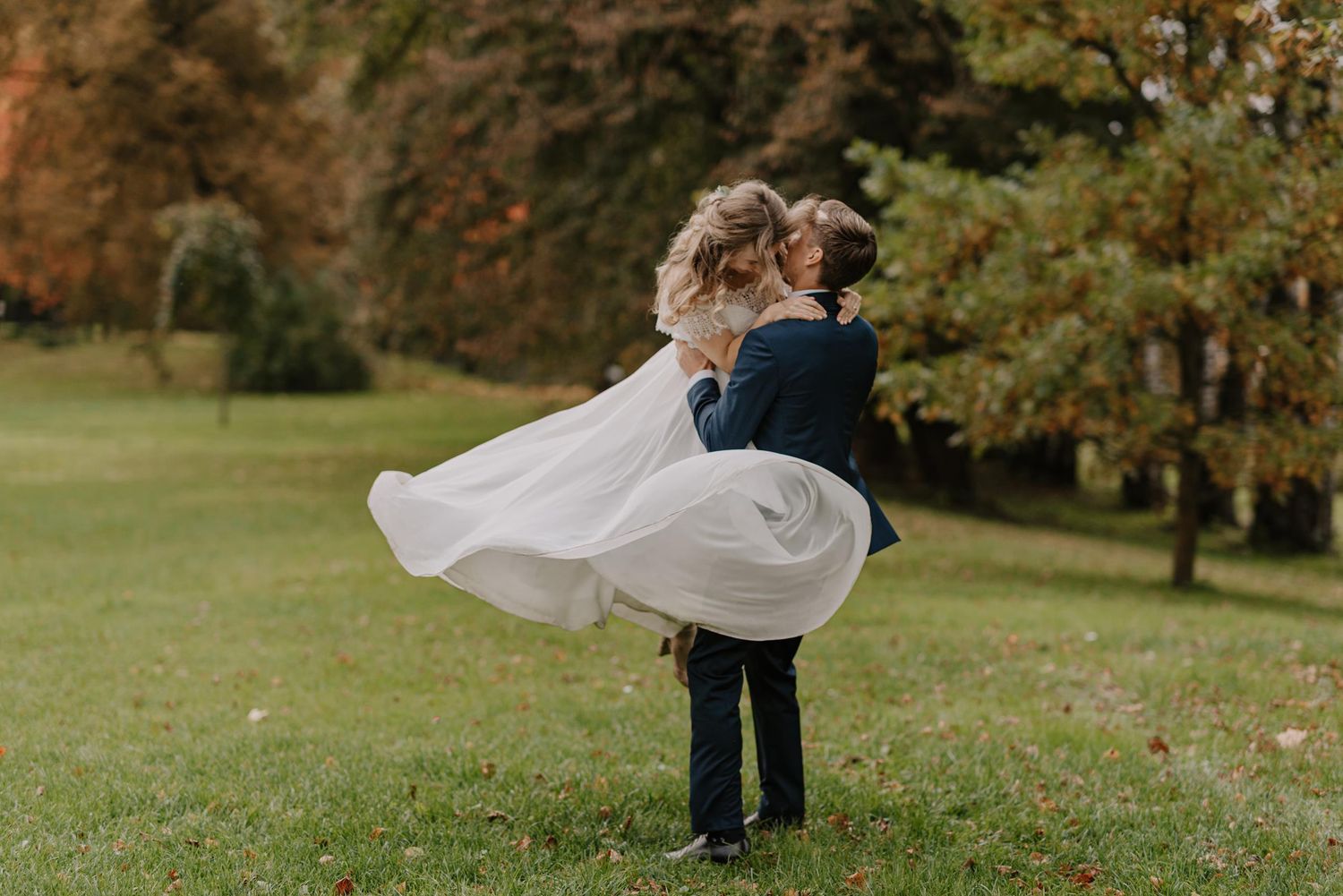 Elegant white wedding dress flows in the breeze as couple moves across garden setting.