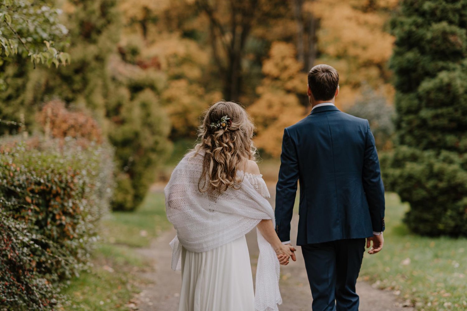 Couple walks hand in hand through garden path surrounded by fall colors.
