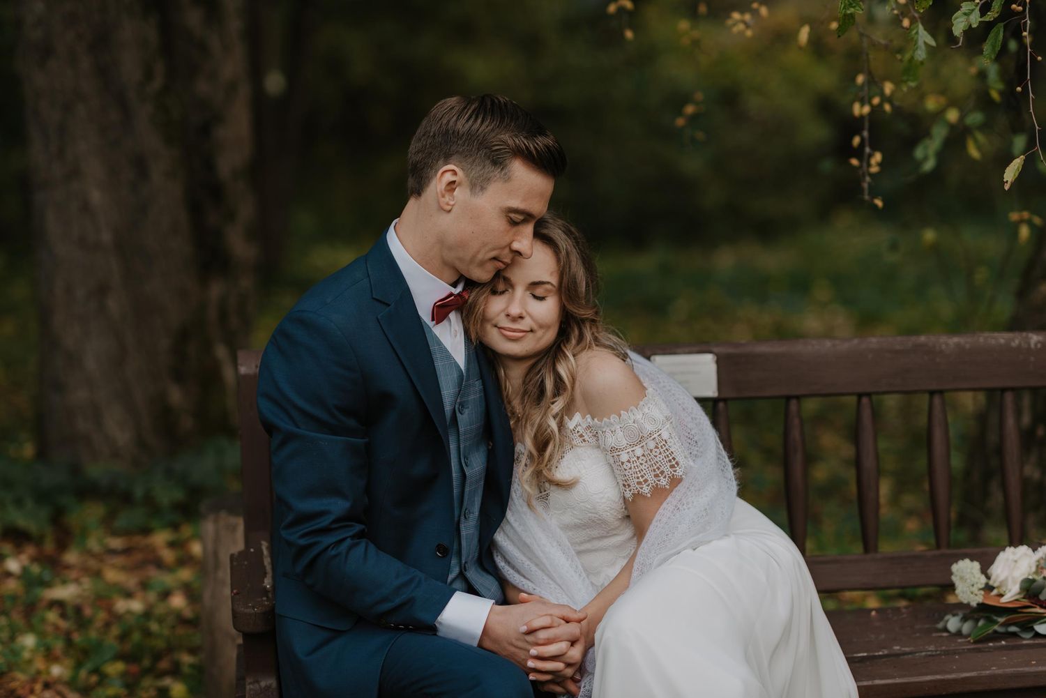Romantic wedding portrait by rustic wooden railing in natural outdoor setting.