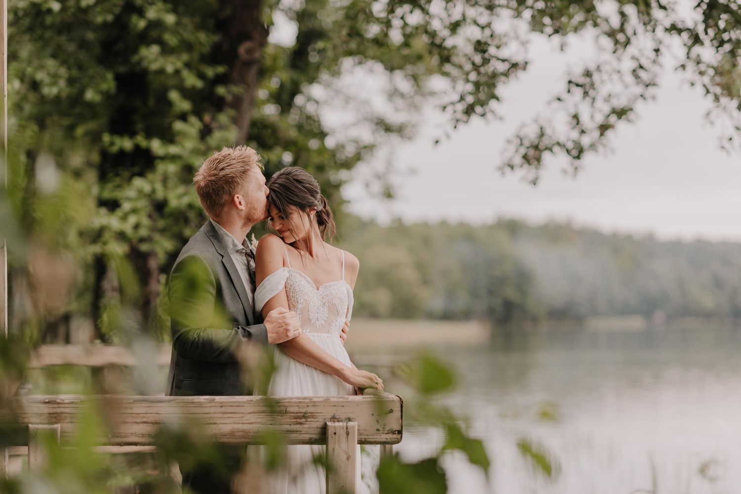 Intimate lakeside wedding moment captured under hanging tree branches.