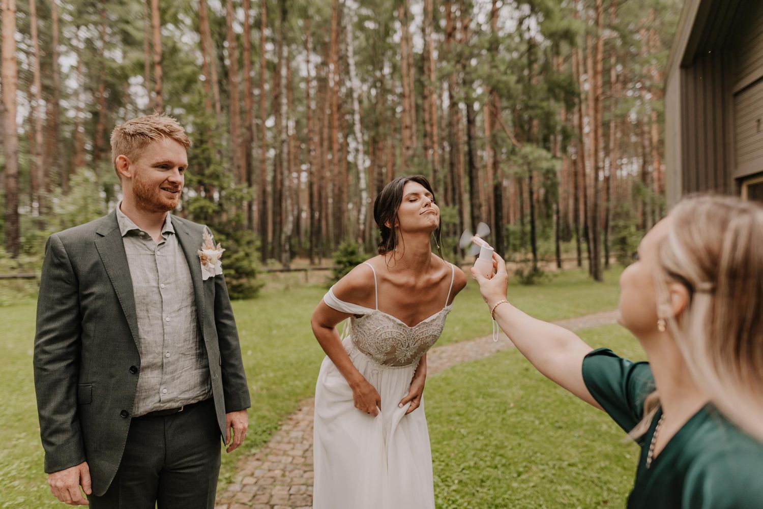 Wedding guests mingling on a lush green lawn surrounded by pine trees.