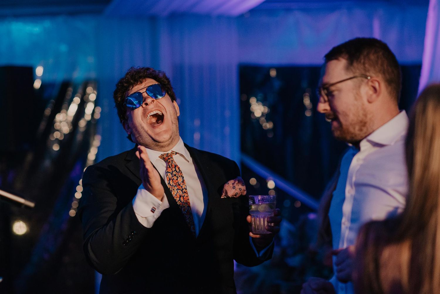 Two guests share an enthusiastic moment at a party with blue ambient lighting.