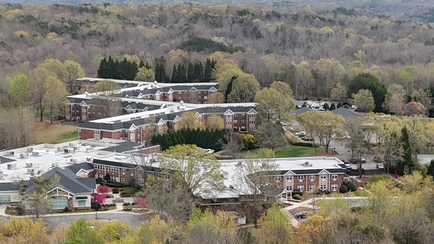Aerial view of a modern commercial complex with multiple buildings nestled in wooded hillside during early spring.