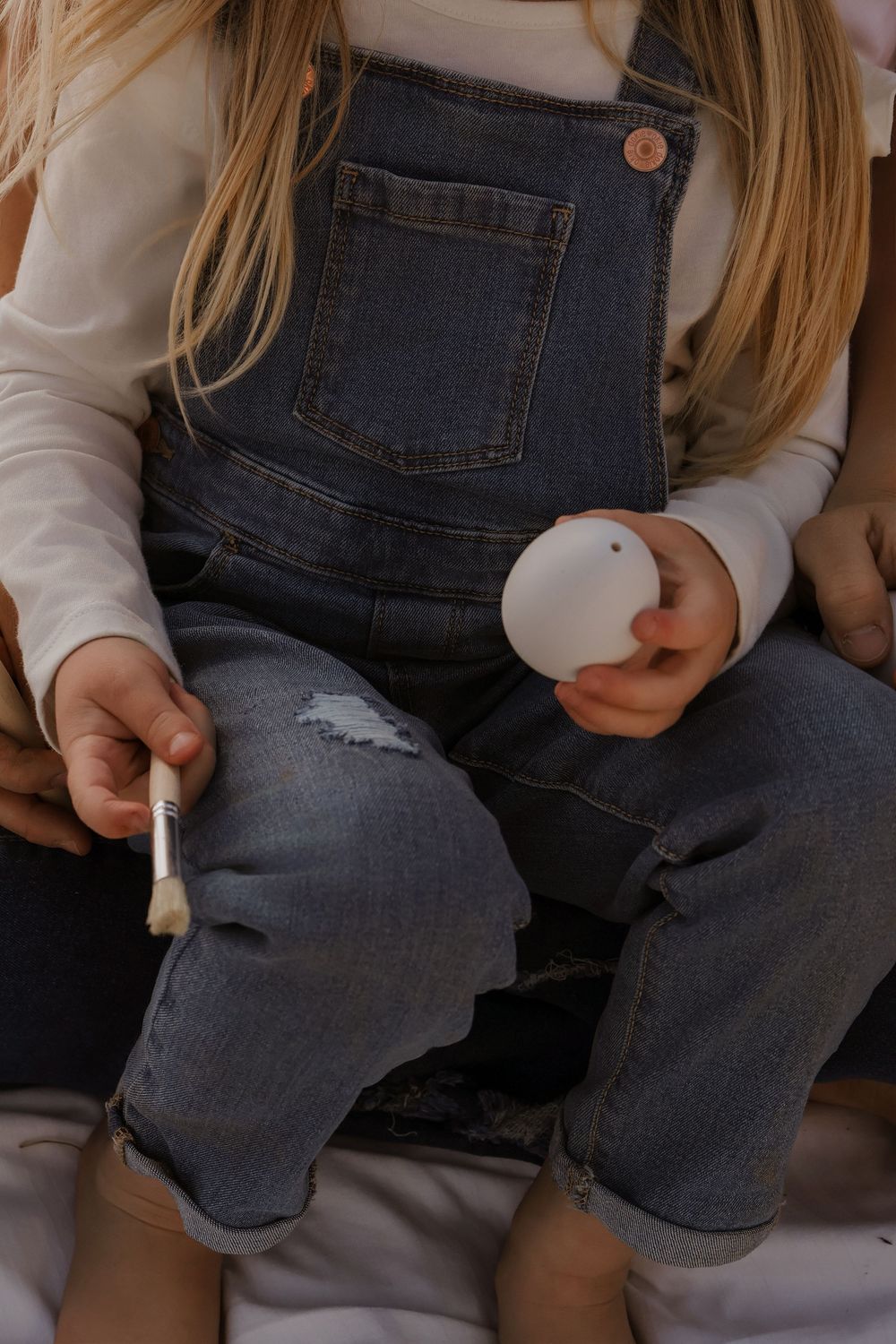 Close-up details of denim overalls and white sweater in natural light setting.