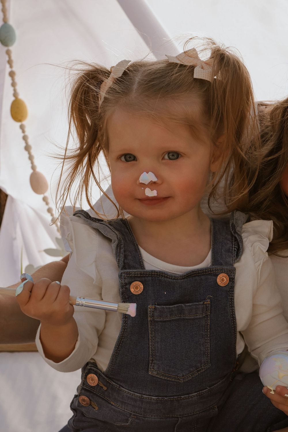 Child in denim overalls and white shirt playing with cotton balls during a photoshoot.