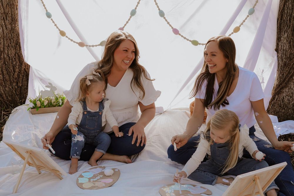 Family sitting on white blanket outdoors for casual photo session.