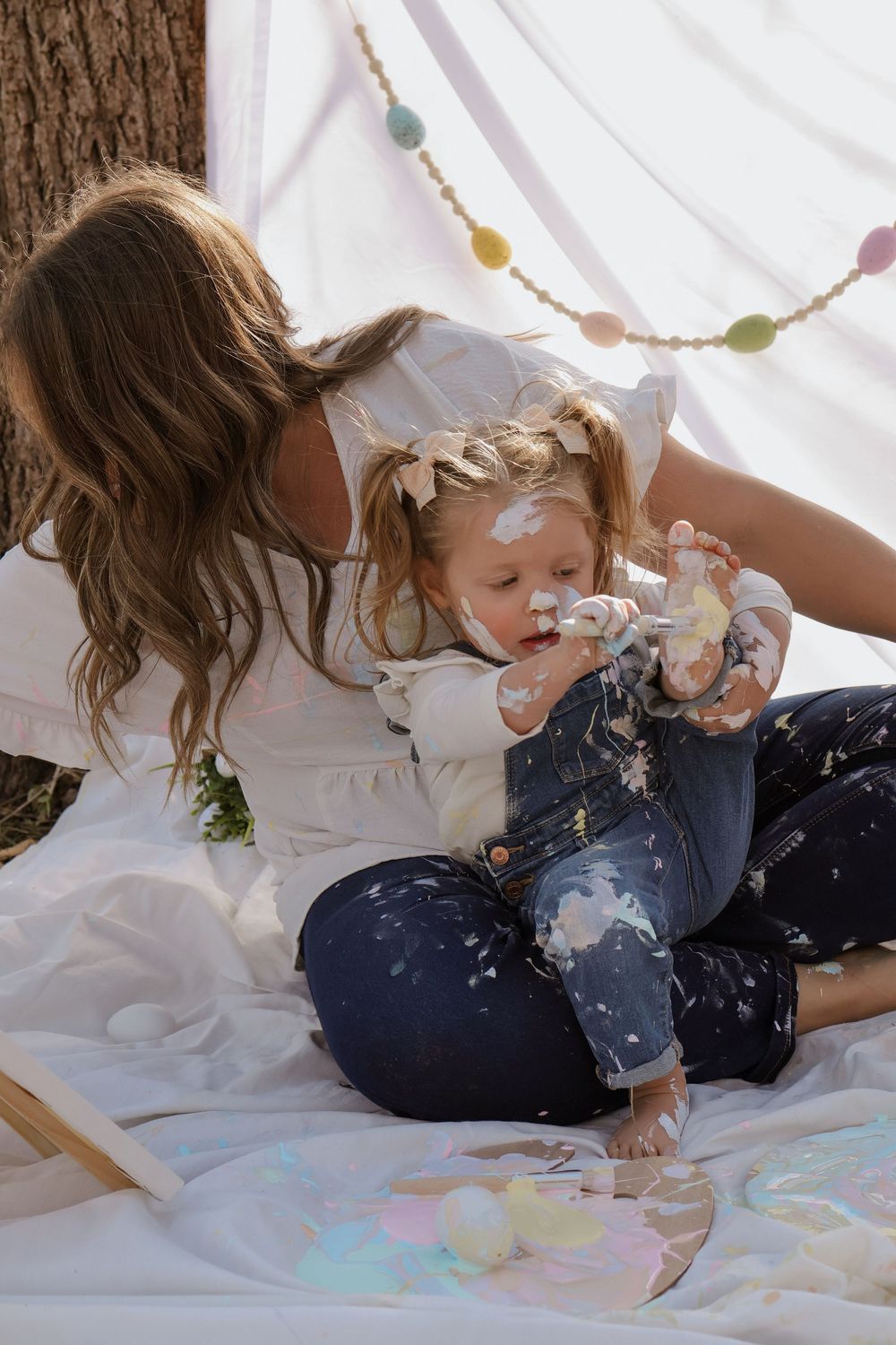 Playful art session with paint and white sheets creating colorful messy fun on the floor.