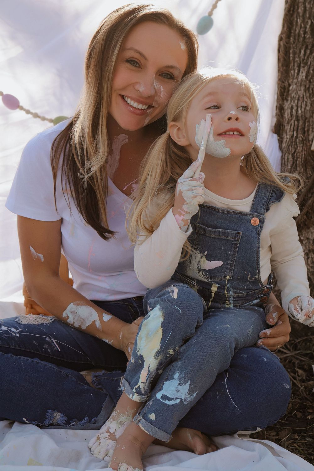 Joyful bonding moment during a messy paint art session against white backdrop outdoors.