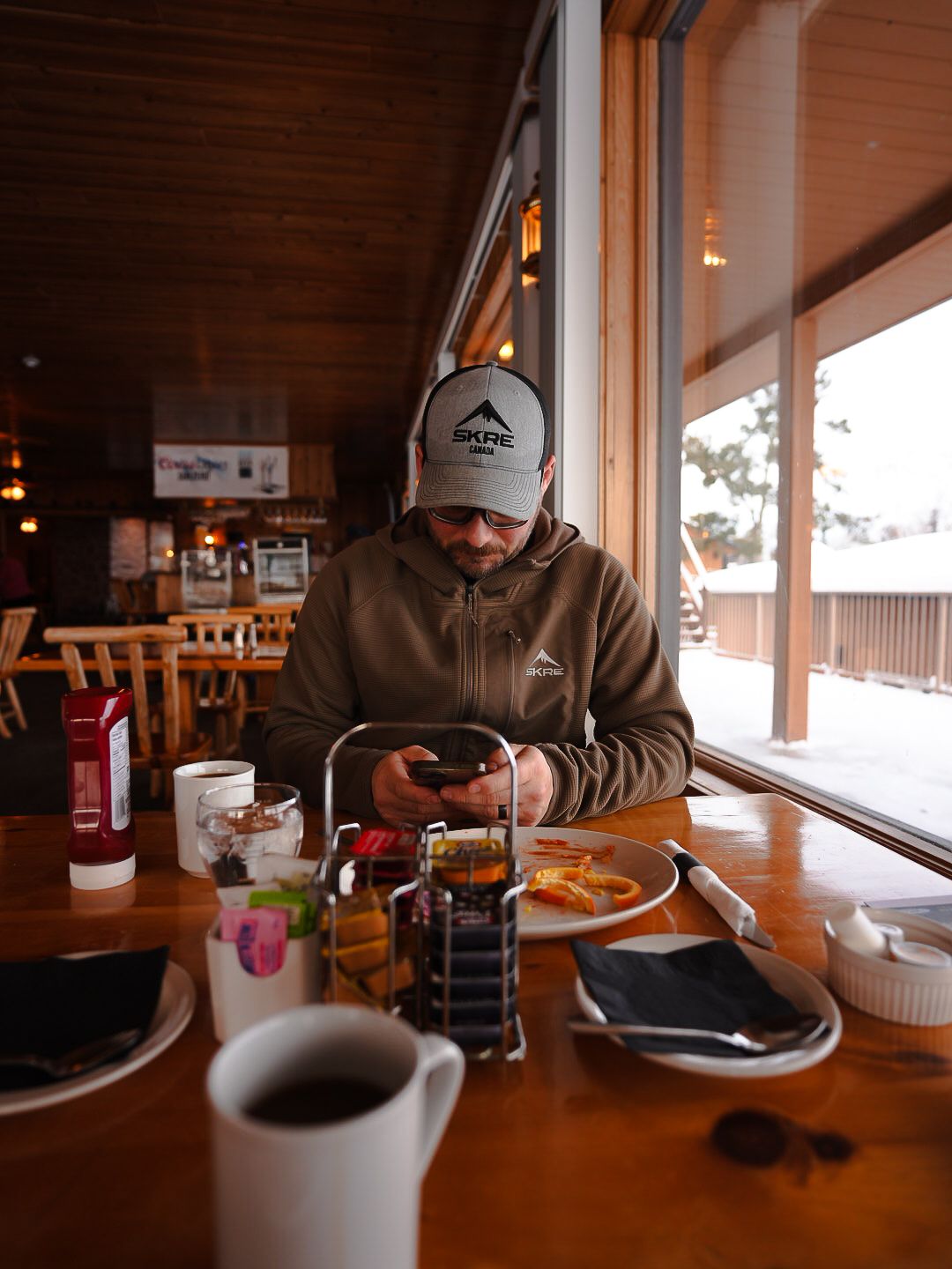 Coffee and food on a rustic wooden table by a window in a cozy restaurant setting.