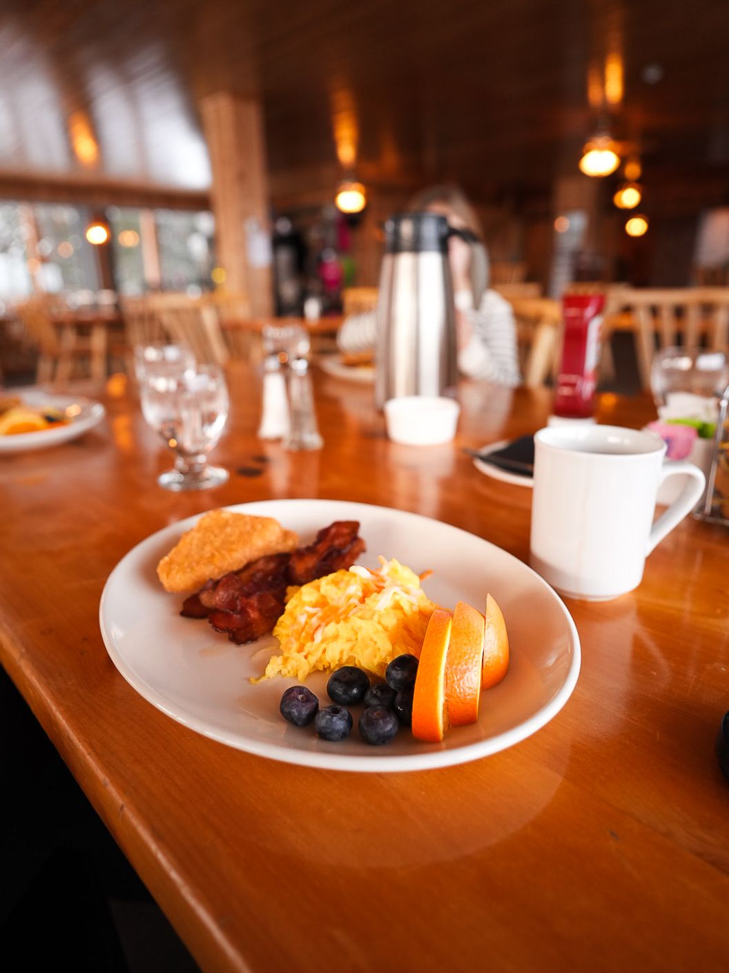 Breakfast plate with eggs, bacon, and fruit served on a wooden table in warm lighting.