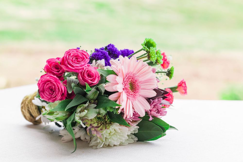 Colorful floral arrangement with pink roses, purple flowers and a pink gerbera daisy on white surface.