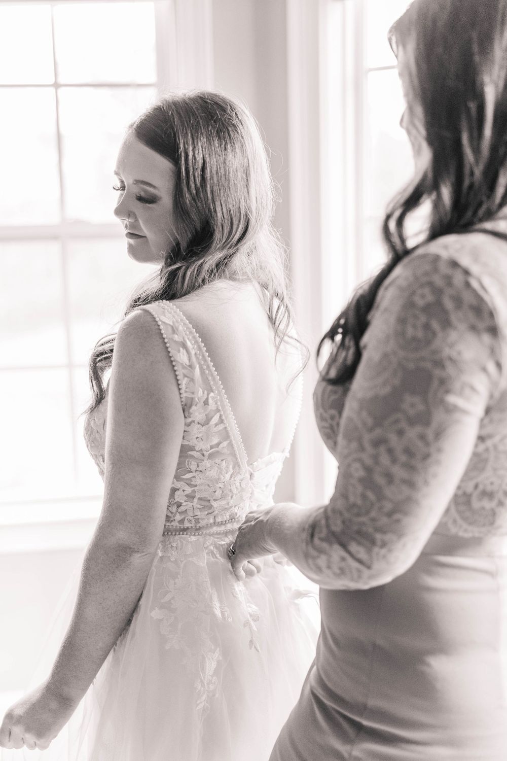 Black and white photograph showing delicate lace details of a wedding dress being adjusted.