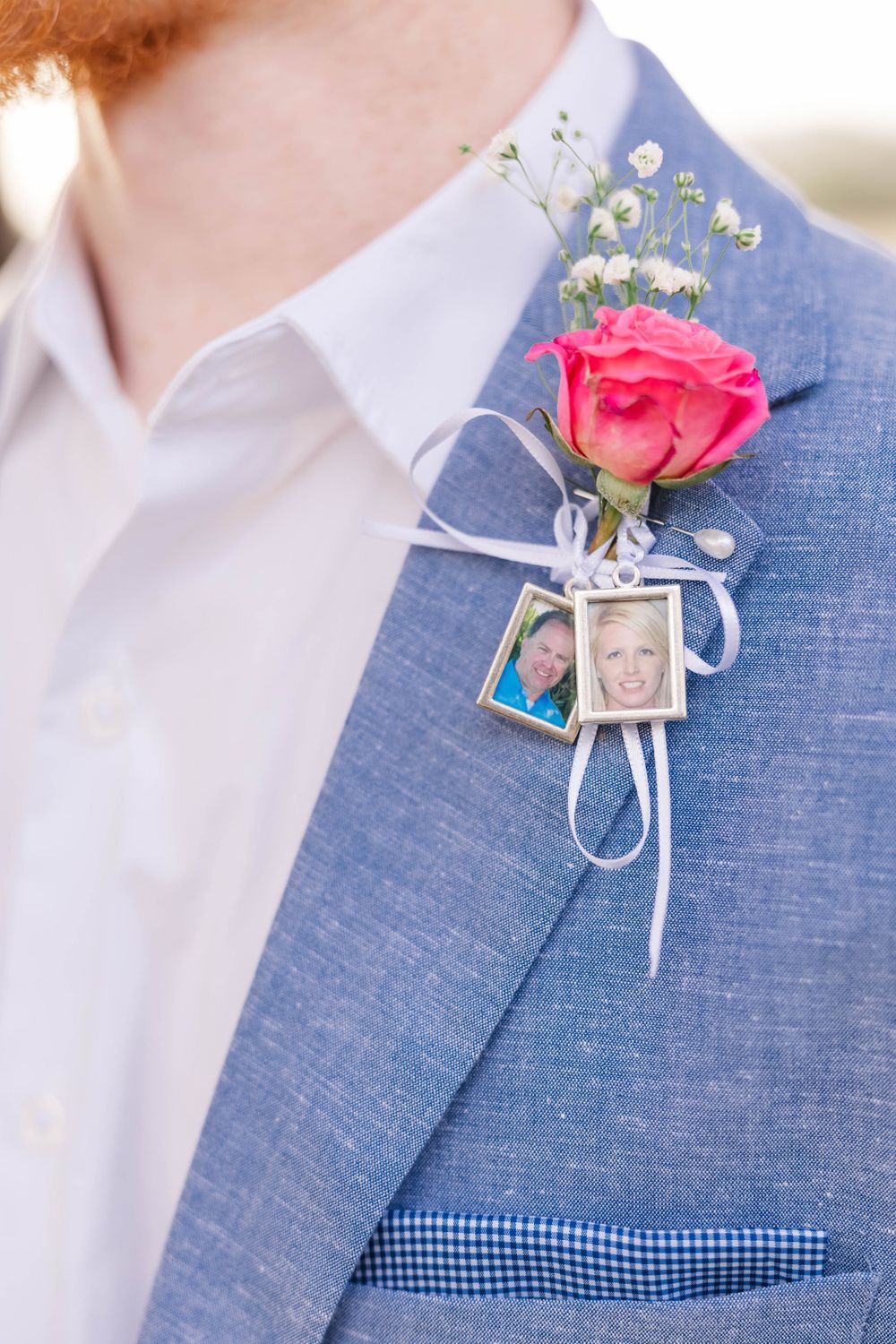 A pink rose boutonniere with baby's breath and small photo charms pinned to a blue suit lapel.