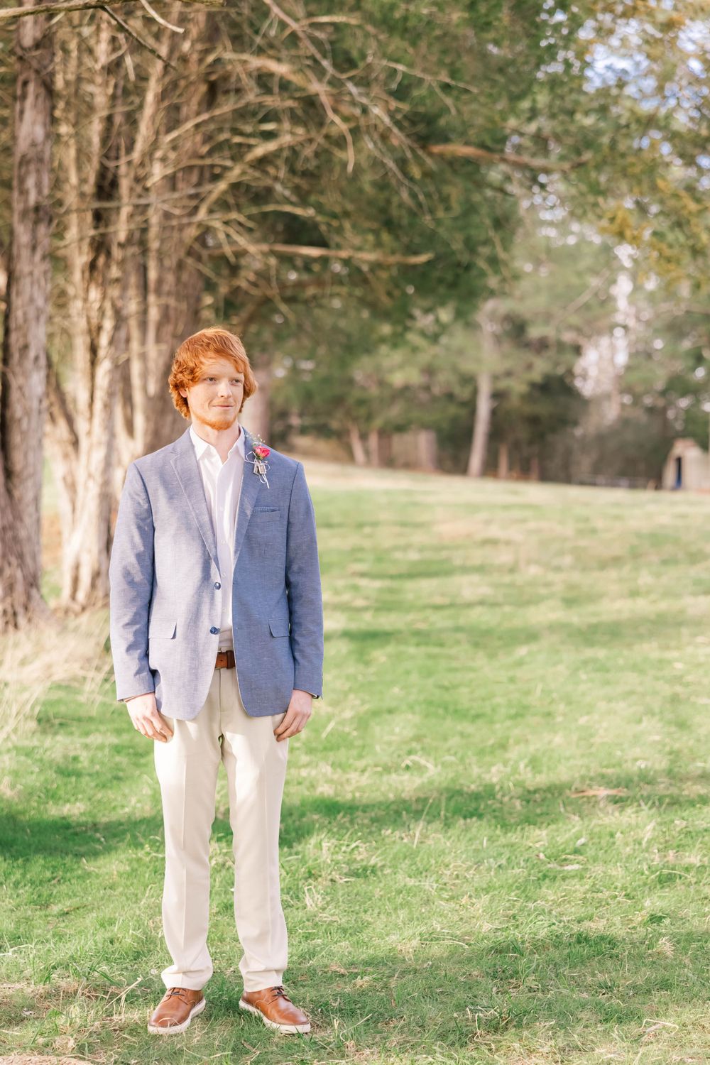 A formal portrait outdoors with trees showing a light blue suit and khaki pants combination.
