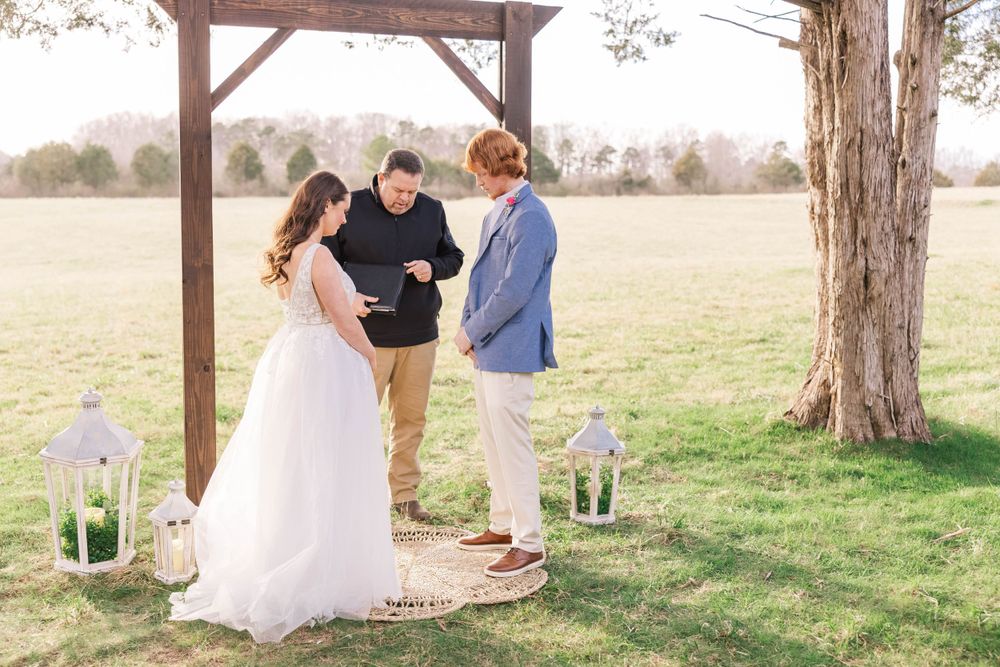 Outdoor wedding ceremony under rustic wooden arbor with decorative lanterns.