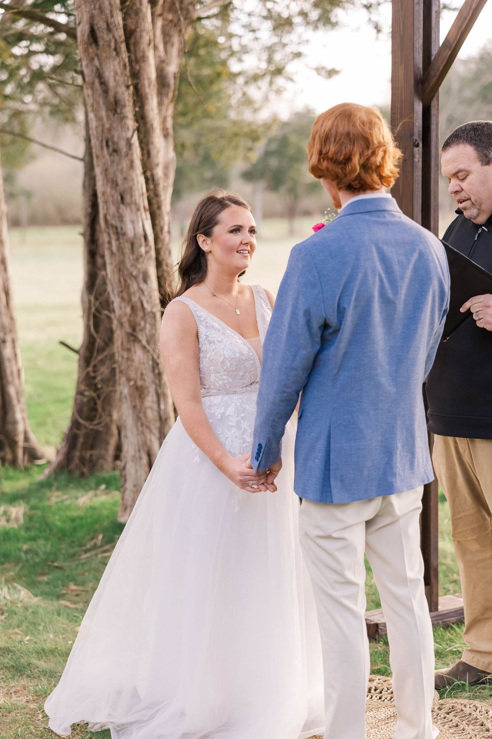 Intimate wedding ceremony moment under wooden pergola with natural landscape backdrop.
