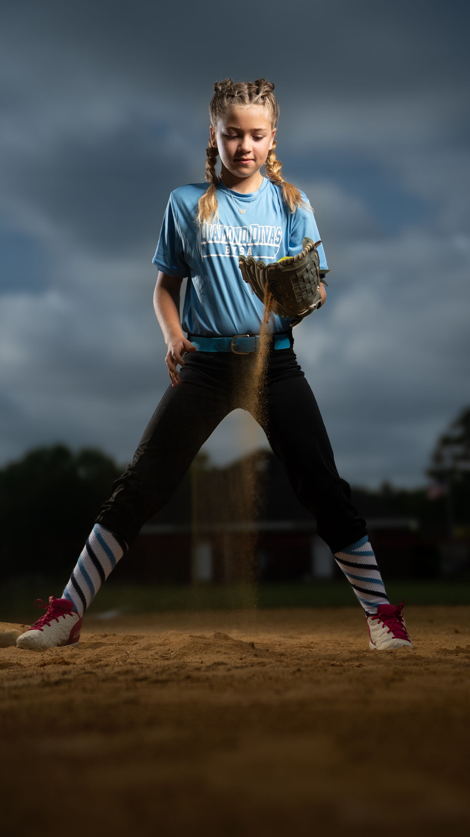Baseball player in black uniform with pink socks stands in batting stance at home plate as dust swirls around cleats.