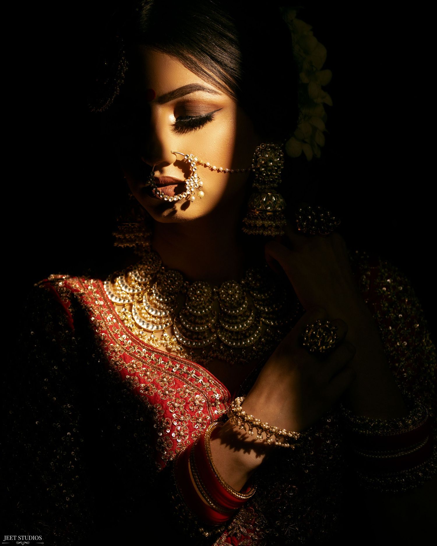 A dramatic portrait in traditional South Asian bridal attire with gold jewelry and red embellishments captured in chiaroscuro lighting.