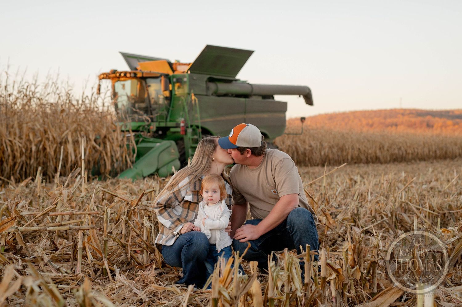 Family bonding moment in harvested cornfield with combine harvester at sunset.