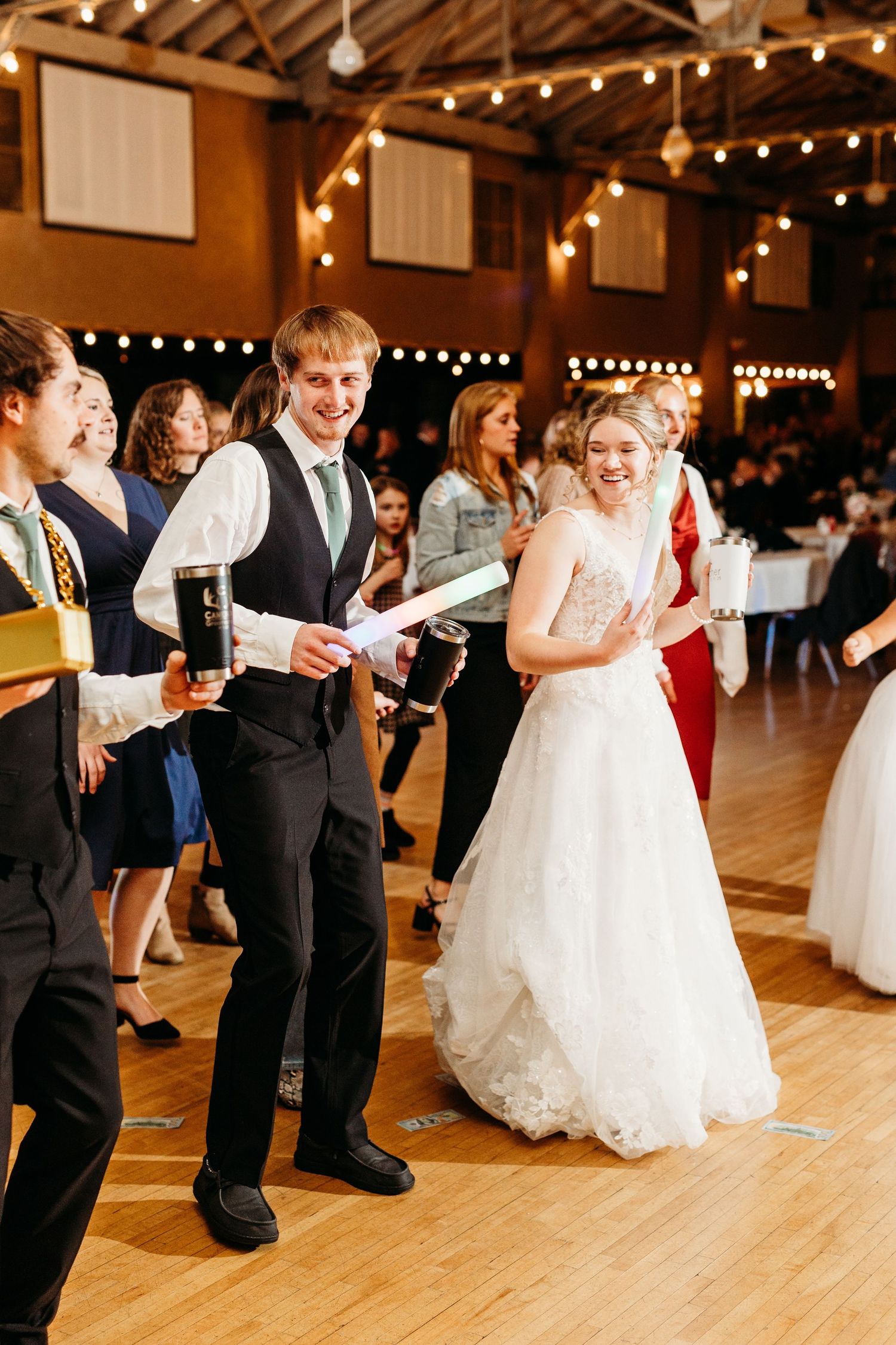 Wedding celebration with joyful dancing and string lights in a rustic venue with wood floors and warm ambiance.