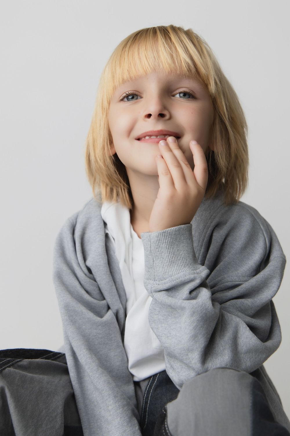 A series of five photos showing a child in a gray hoodie making playful expressions against a white background.