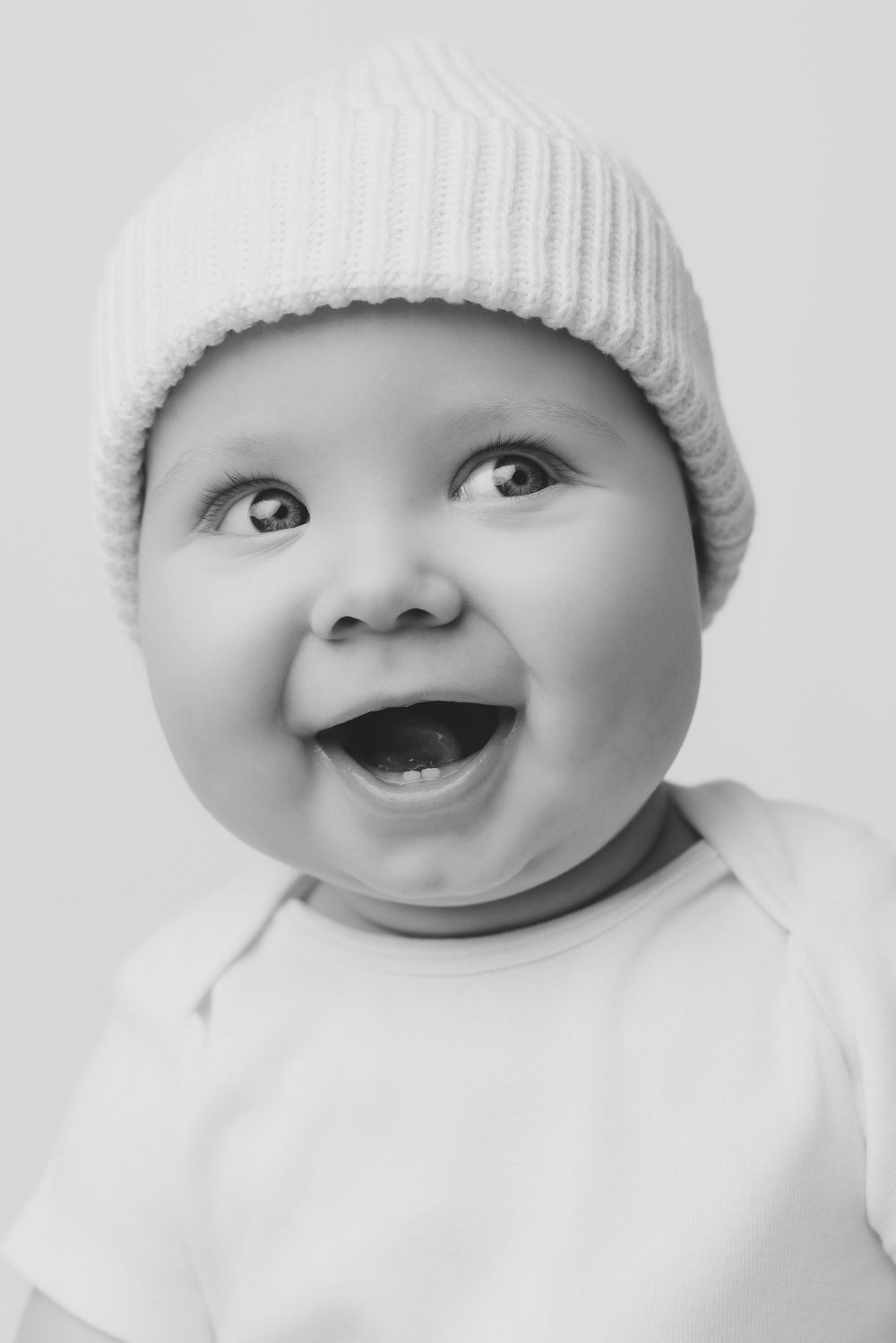 Black and white portrait of a happy smiling baby wearing a knit hat.