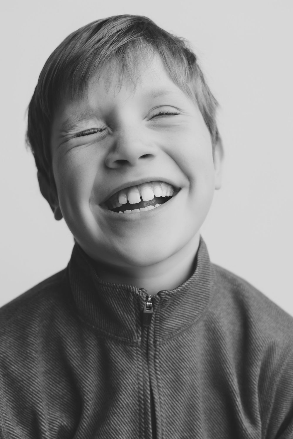 Black and white portrait of a laughing boy with eyes closed, wearing a zip-up jacket, radiating pure joy.