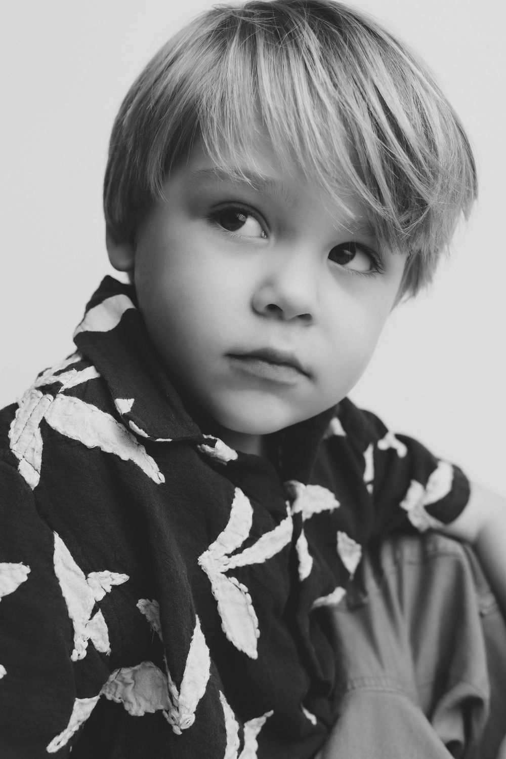 Black and white portrait of a young blonde boy wearing a leaf-patterned shirt, looking thoughtfully to the side.