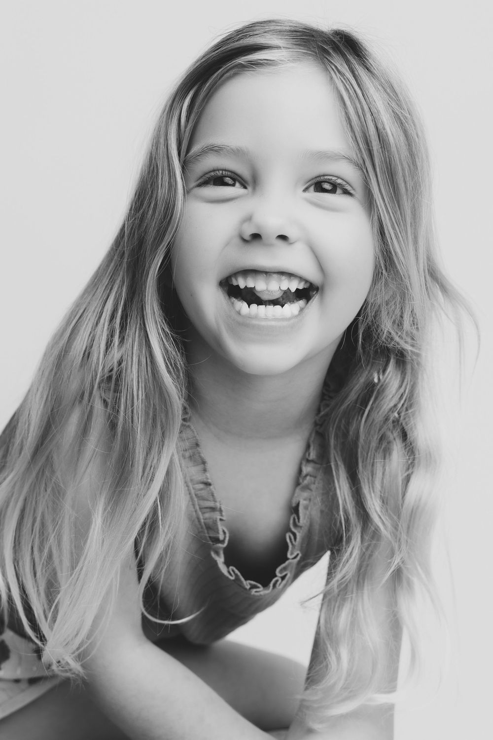 Black and white portrait of a joyful young girl with long blonde hair laughing and smiling brightly.
